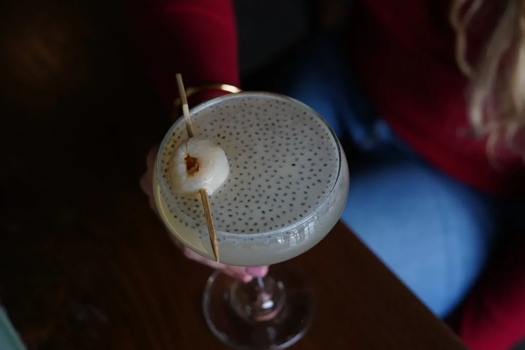 A lychee and chia seed drink in a coupe glass.