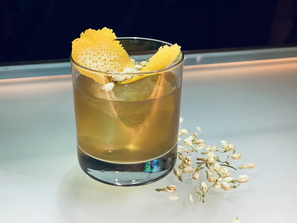 A cocktail with lemon peel and flowers, next to dried flowers.