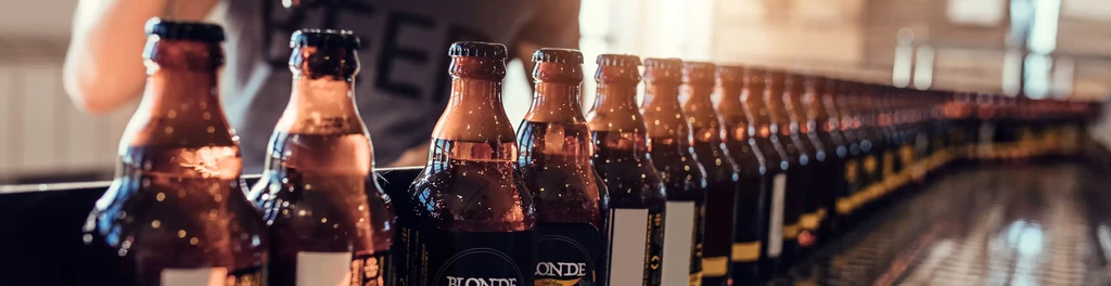 Rows of brown beer bottles moving along a conveyor belt.