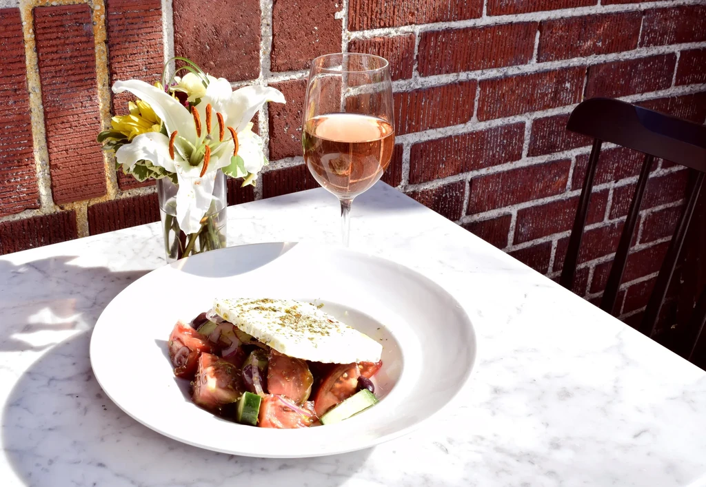 Salad, rose wine, and flowers on a white marble table outdoors.