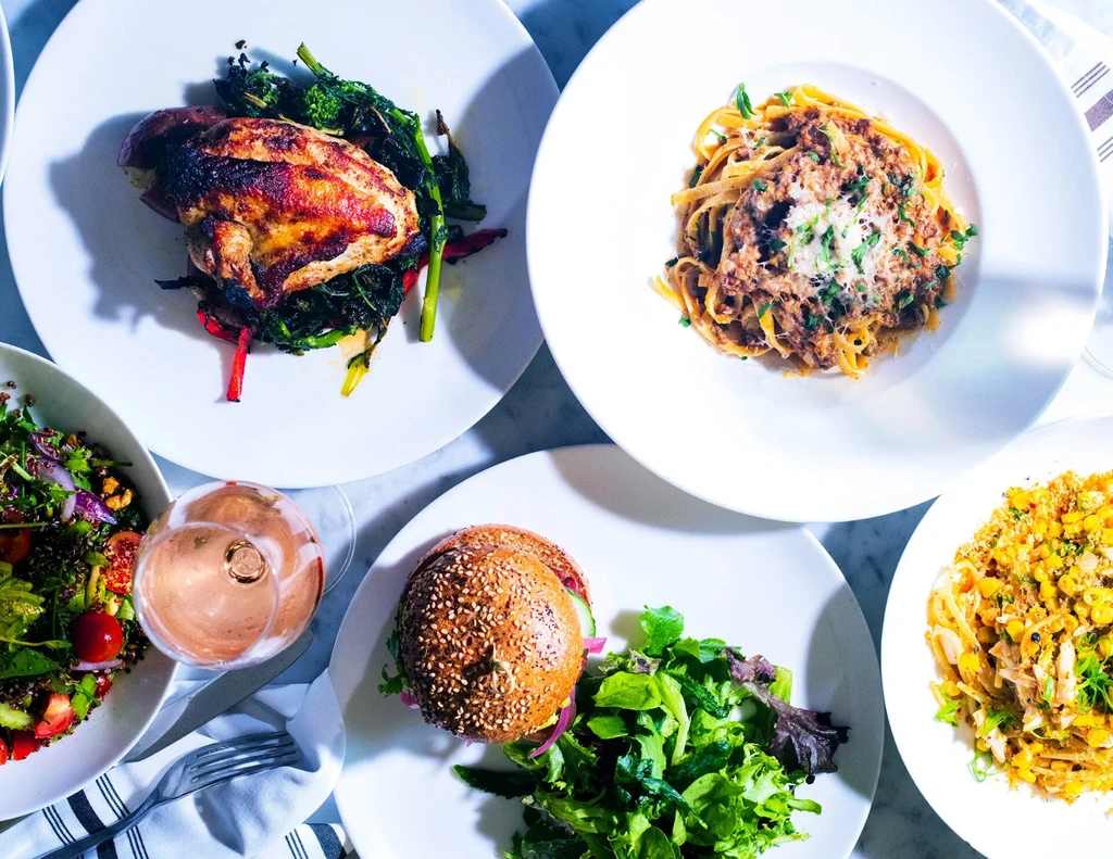 Assortment of plated dishes: chicken, pasta, burger, salad, and corn pasta.