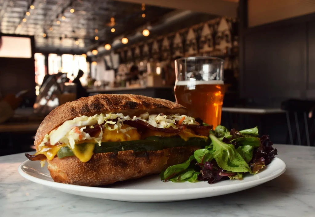 A sandwich with a side salad and beer on a table in a restaurant.