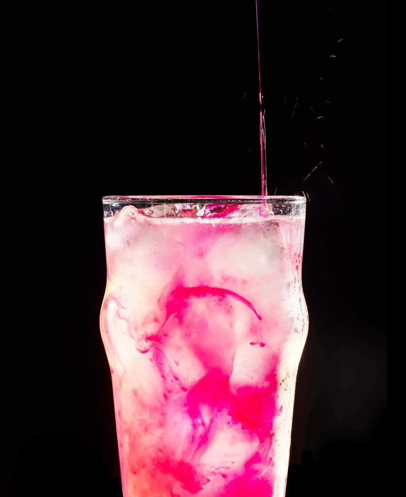 Pink liquid pours into an ice-filled glass against a black background.