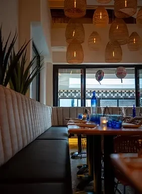 A warmly lit restaurant interior with wicker lamps and blue water bottles.