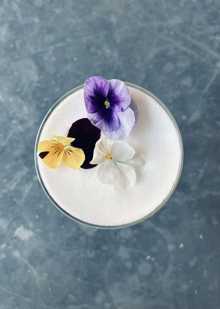 A white cocktail with three pansy flowers on a blue background.
