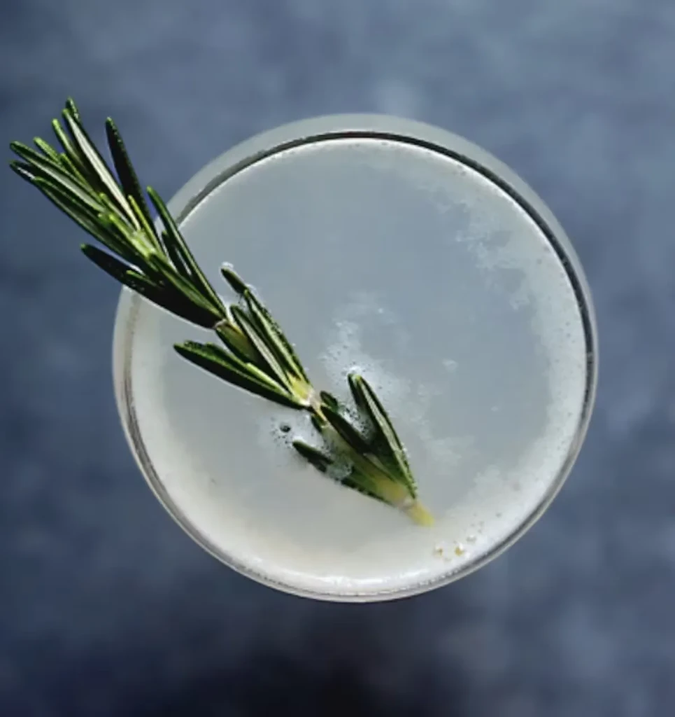 An overhead shot of a light-colored cocktail with a rosemary sprig.