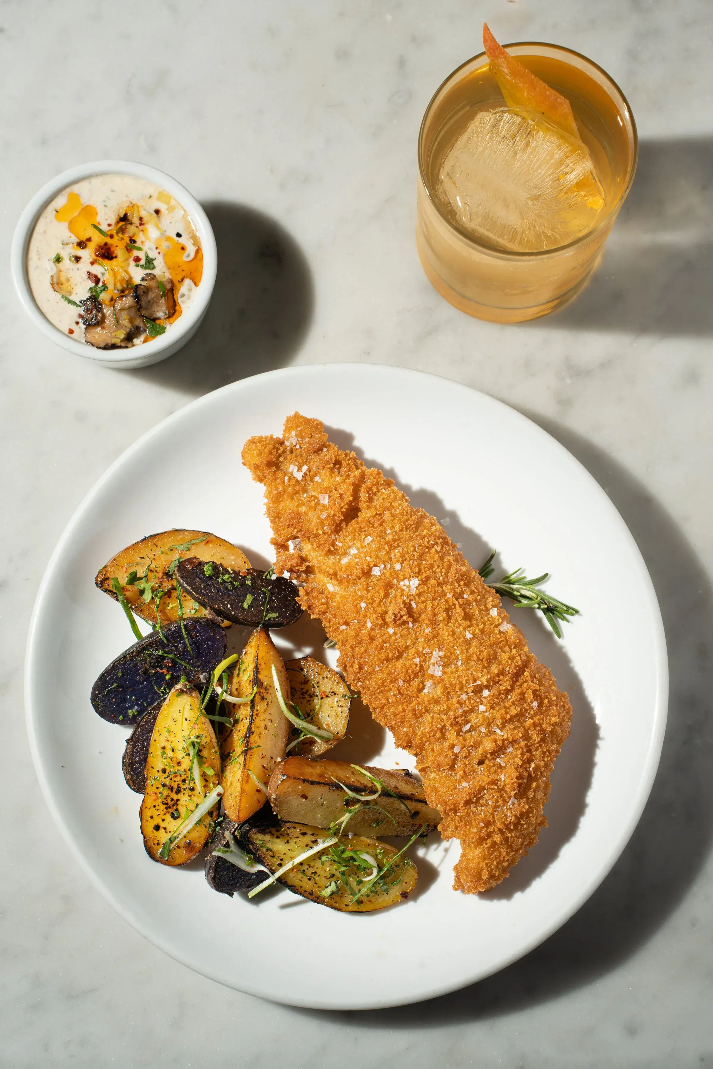 Fried fish with potatoes, dip, and cocktail on marble surface.