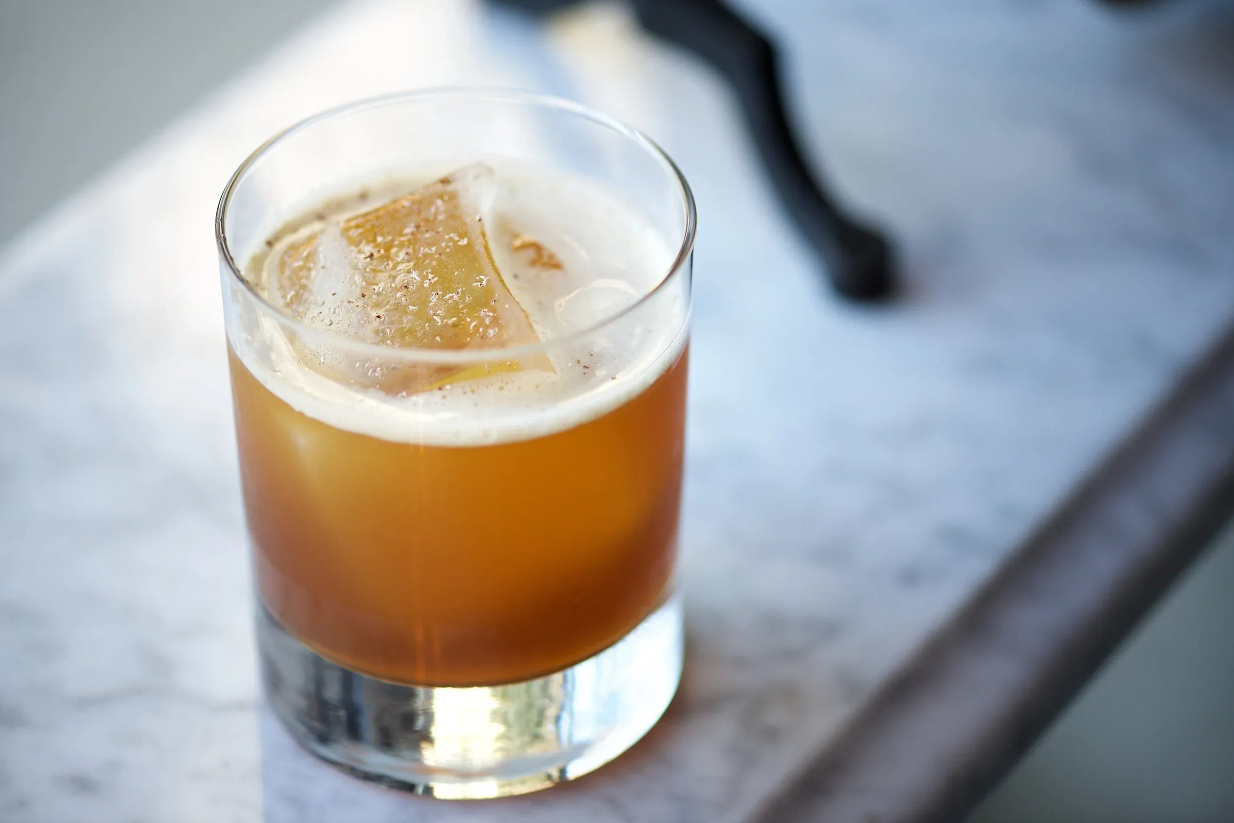 An orange-brown cocktail in a glass with ice, garnished with spice.