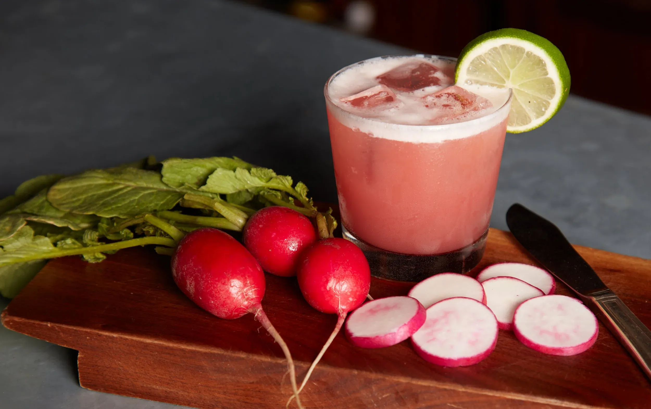 Radishes, sliced radishes, a knife, and a pink drink.