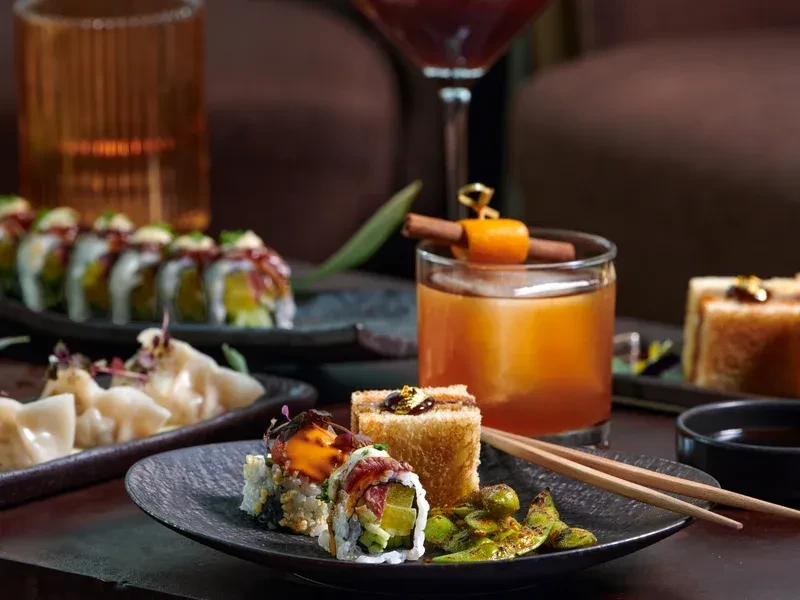 Sushi, dumplings, cocktails, and edamame served on dark plates.
