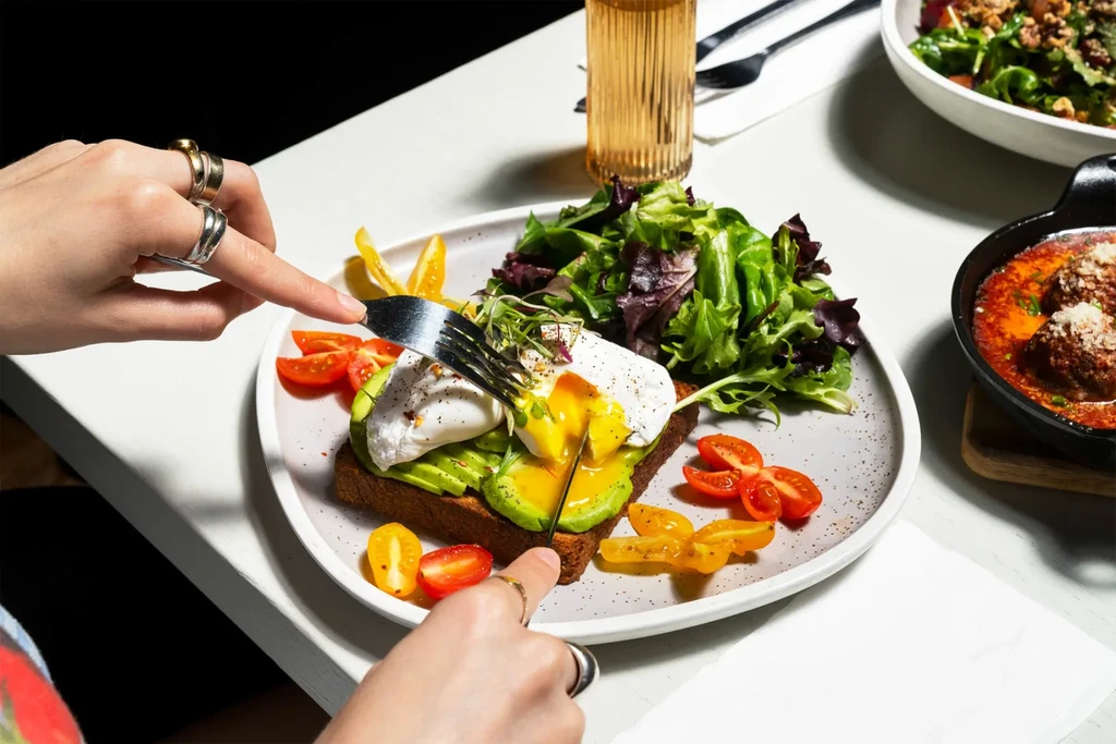 A person cuts into avocado toast with a poached egg.