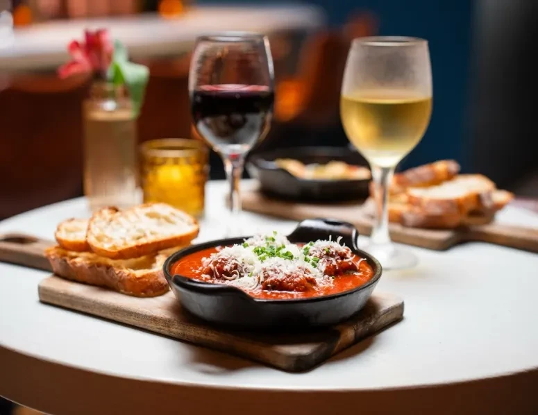 A table with red and white wine, meatballs, and bread.