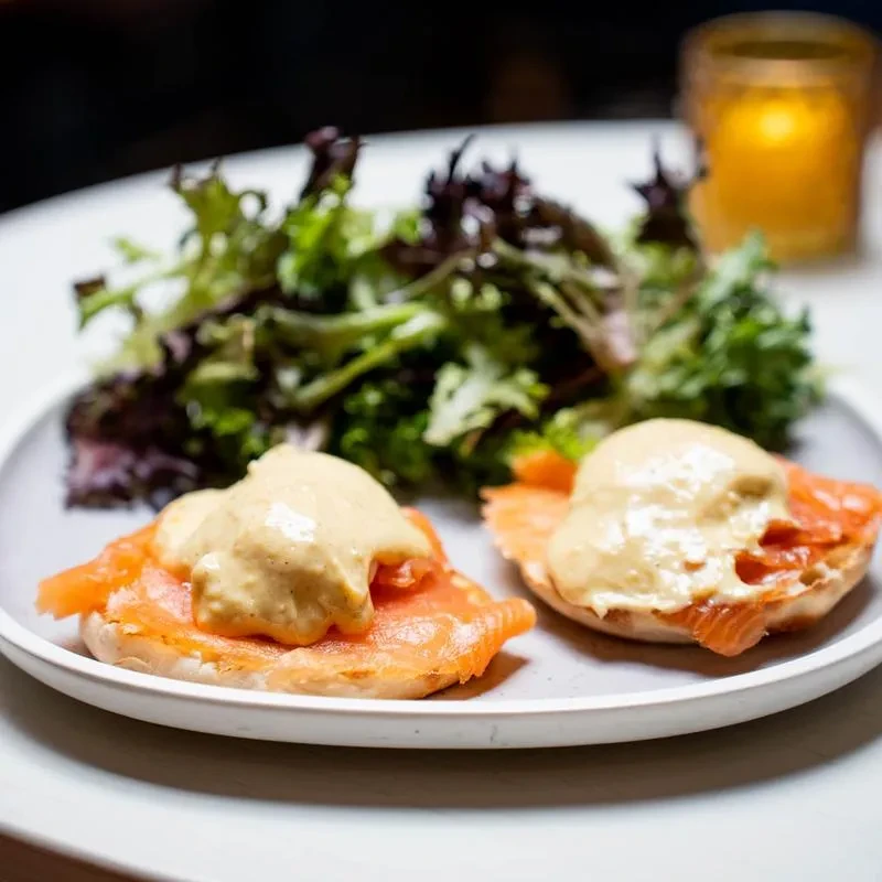 Two bagels with salmon, hollandaise, and a side salad.