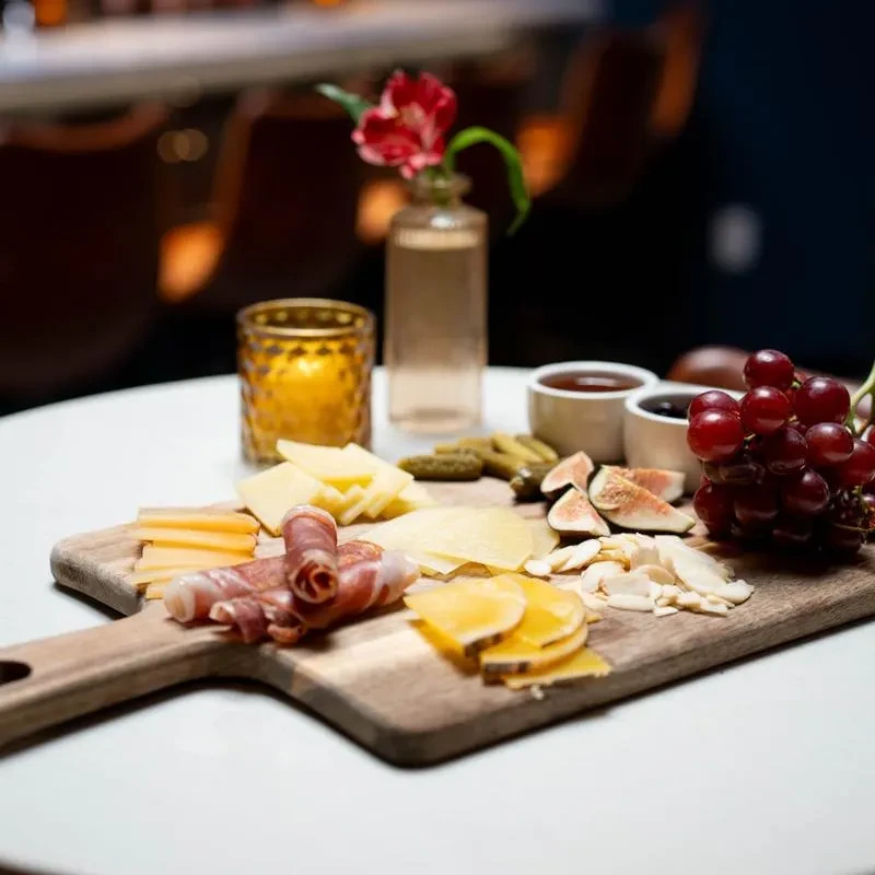 Charcuterie board with cheese, prosciutto, figs, grapes, and pickles.