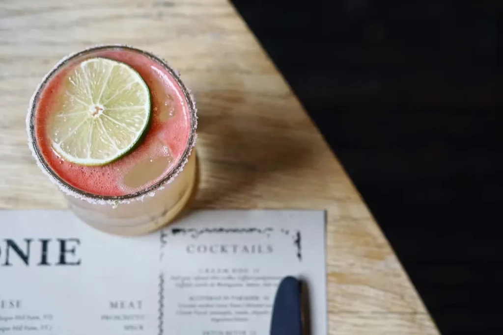 Pink cocktail with a lime slice, salt rim, and a menu.