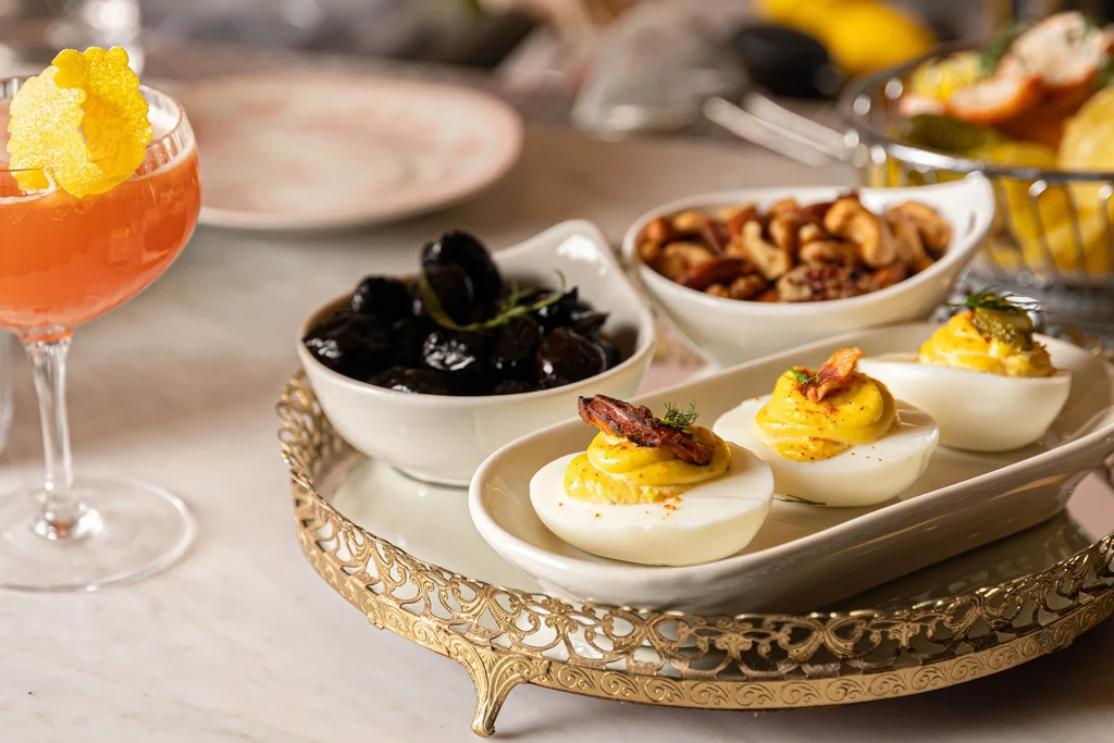 A brass tray with olives, nuts, deviled eggs, and a cocktail.