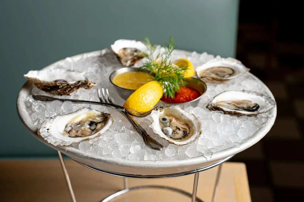 A dozen oysters on a platter of ice with lemon and sauce.