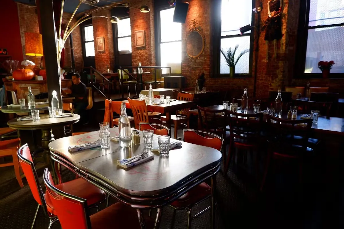 A restaurant interior with brick walls, metal tables, and red chairs.