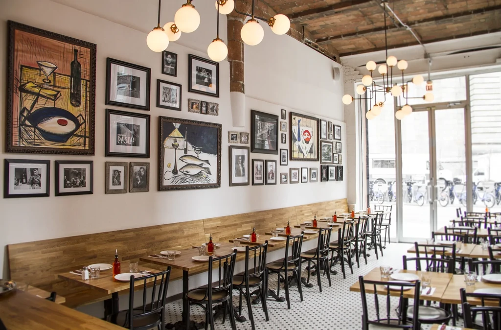 A modern restaurant with a long bench and gallery wall of framed art.
