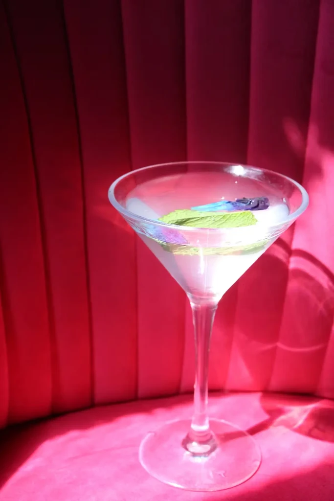 A cocktail garnished with mint and flowers on a pink velvet seat.