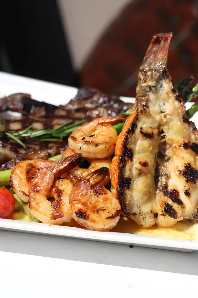 Grilled shrimp, lobster tail, and lamb chops on a white plate.