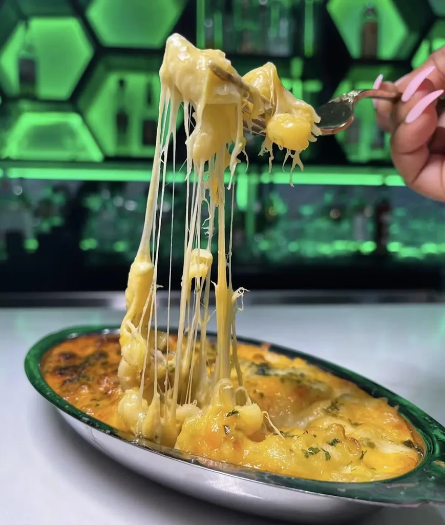 A fork lifts cheesy pasta from a dish, creating long cheese strings.