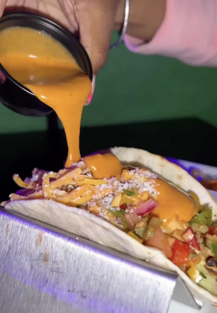 Sauce being poured onto a taco with cheese and salsa.