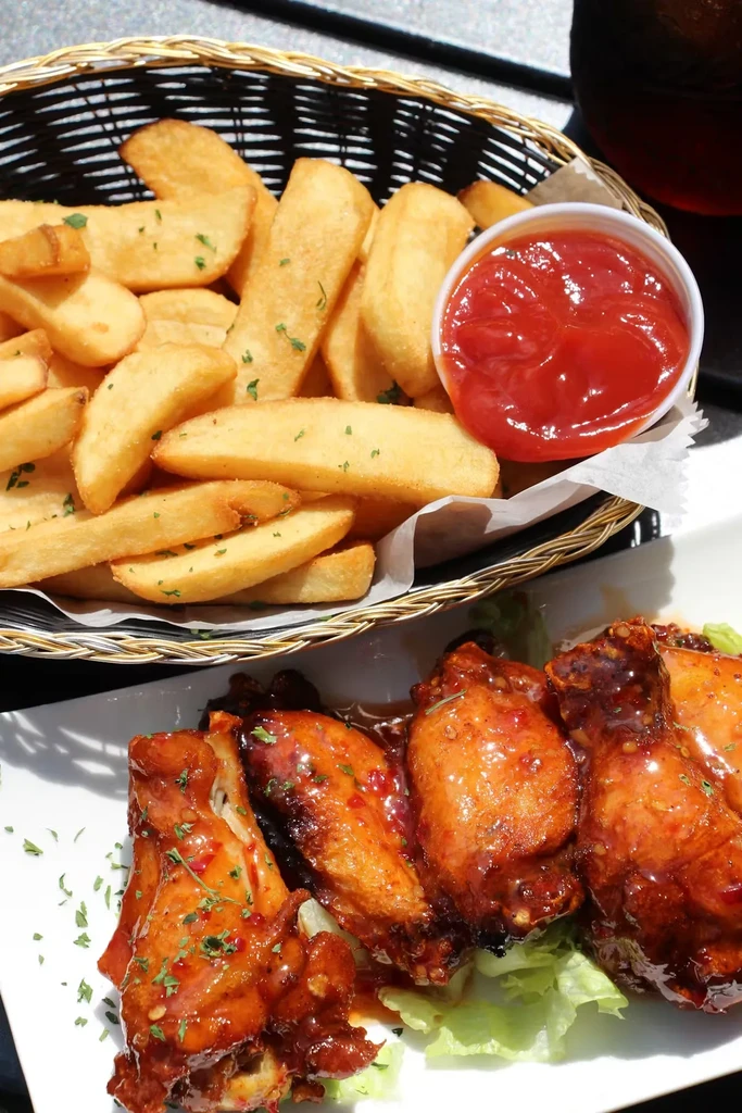 A woven basket of fries with ketchup next to BBQ chicken wings.
