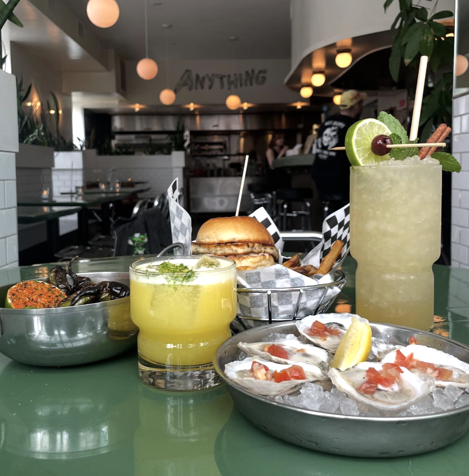 Table with oysters, burger, and cocktails in a restaurant.
