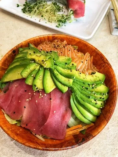 A wooden bowl with salmon, tuna, and avocado slices with sesame seeds.