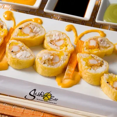 Shrimp tempura sushi rolls on a white plate with orange sauce.