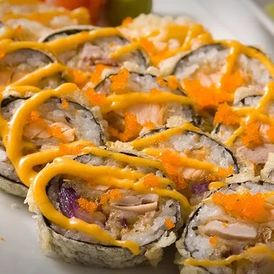 Fried sushi rolls with orange roe and yellow sauce on a white plate.