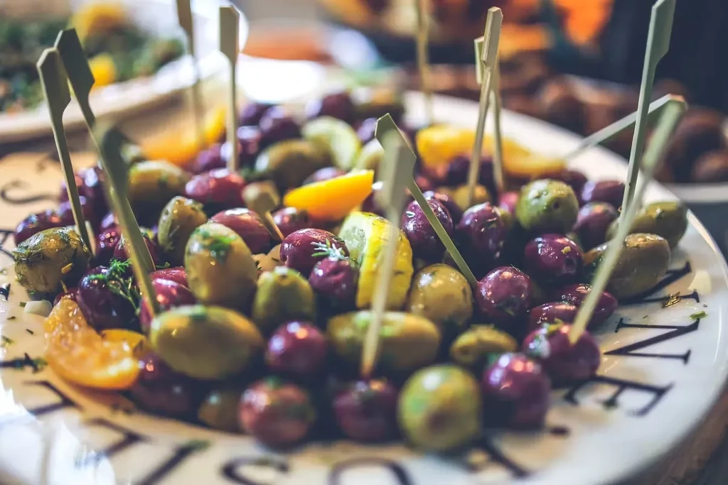 A white plate filled with green and purple olives with toothpicks.