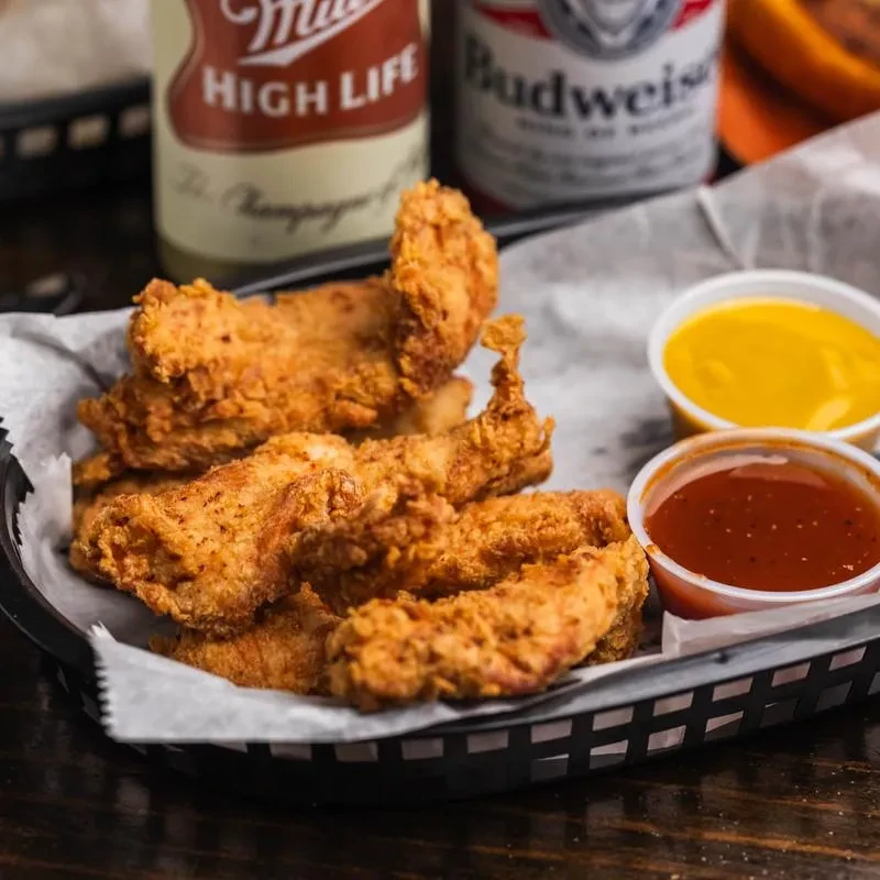 Fried chicken tenders with mustard and hot sauce, two beer bottles.