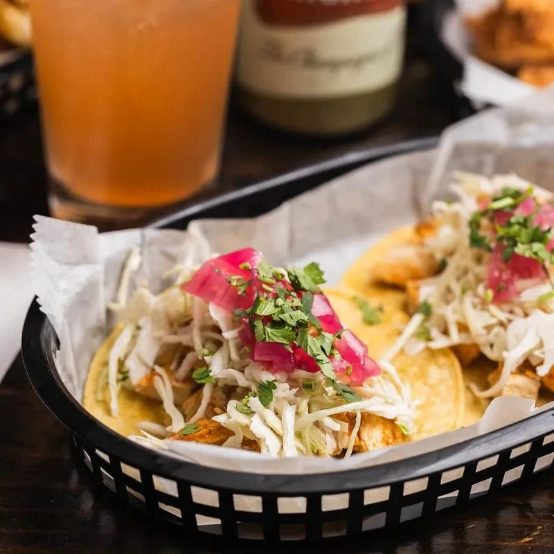 Two chicken tacos with slaw and pickled onions in a black basket.