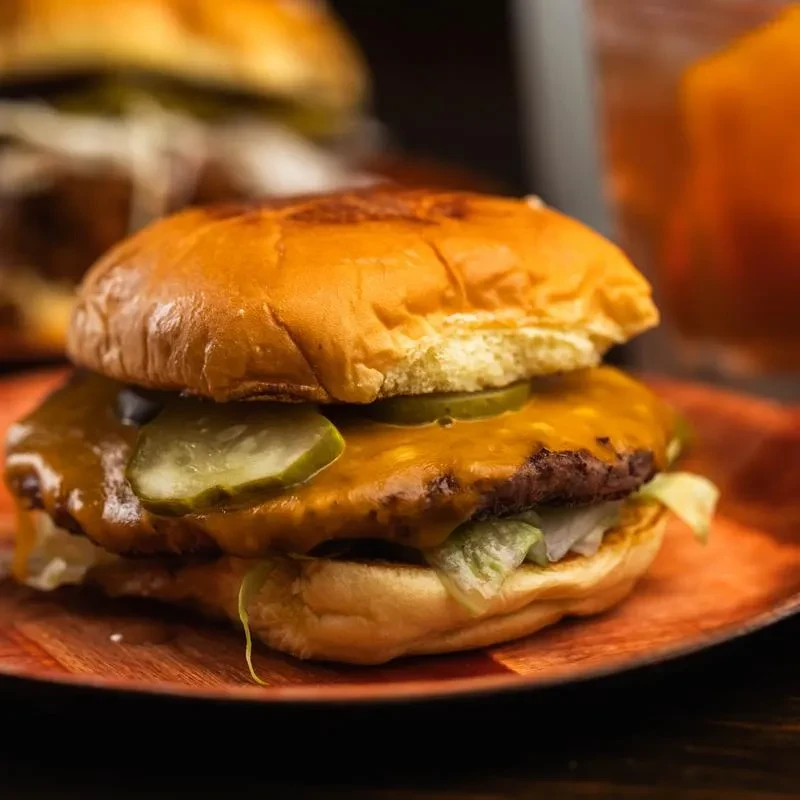 A cheeseburger with pickles and lettuce on a wooden plate.