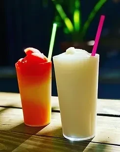 Two tall frozen drinks, one orange-red and one white, with straws.