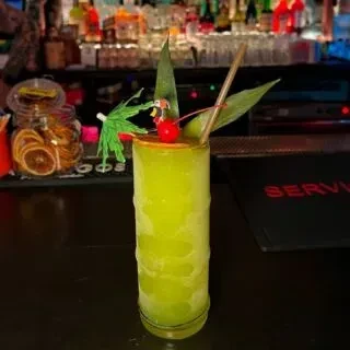 A green cocktail garnished with leaves, a cherry, and an umbrella.