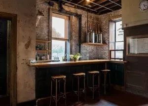 A rustic bar with three stools and exposed brick walls.