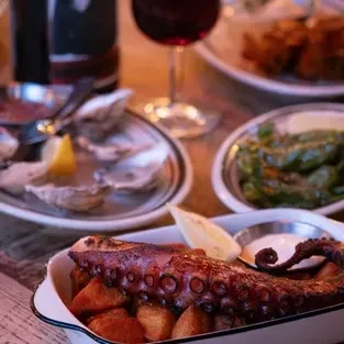 Cooked octopus tentacle on potatoes, oysters, and other dishes on a table.
