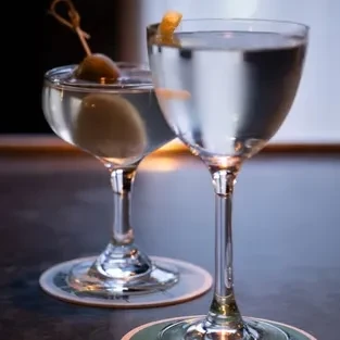 Two clear cocktails, one with an olive, the other with a lemon twist.