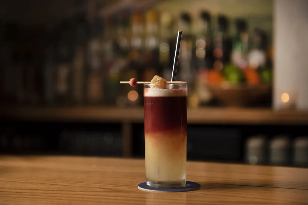 Layered cocktail with straw and garnish on a bar counter.