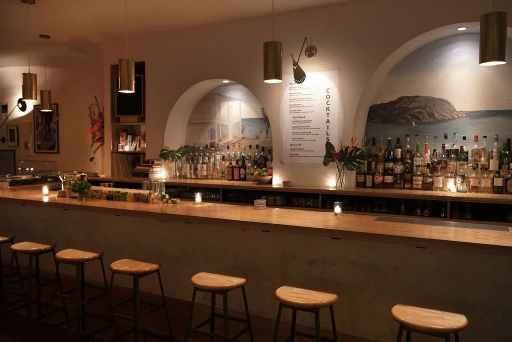 A long, dimly lit bar with stools and bottles of liquor.