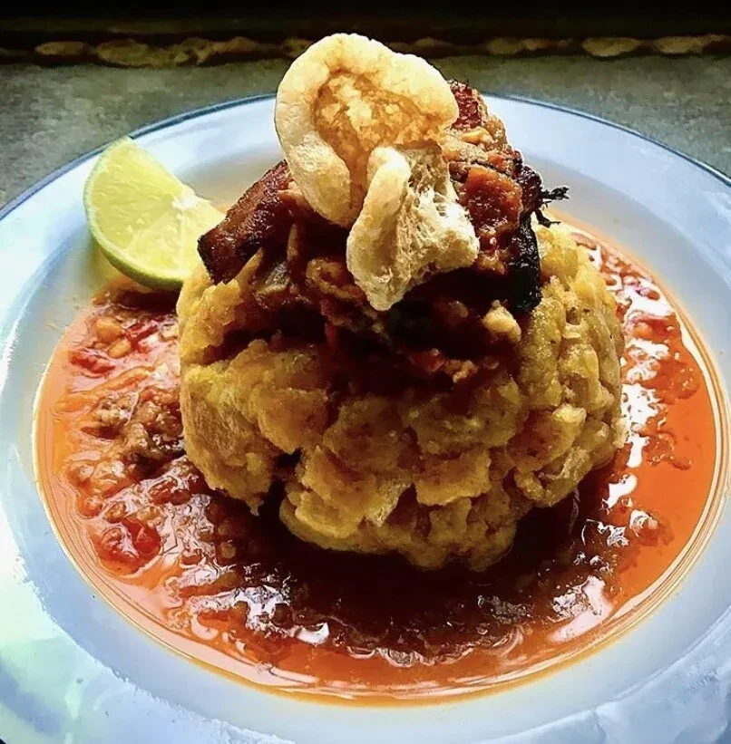 Mofongo served with a red sauce, pork rinds, and a lime wedge.