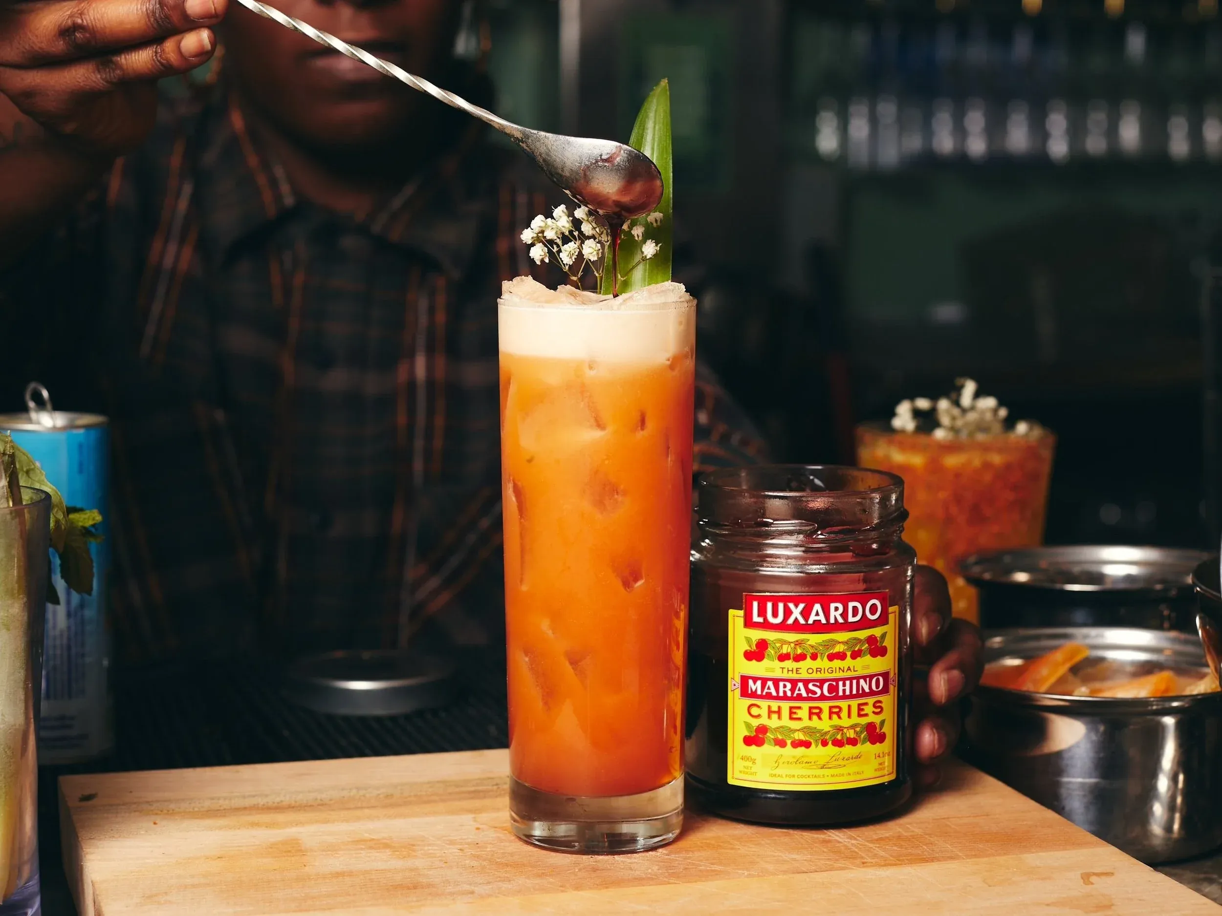 A bartender drizzles syrup from a spoon onto an orange cocktail.