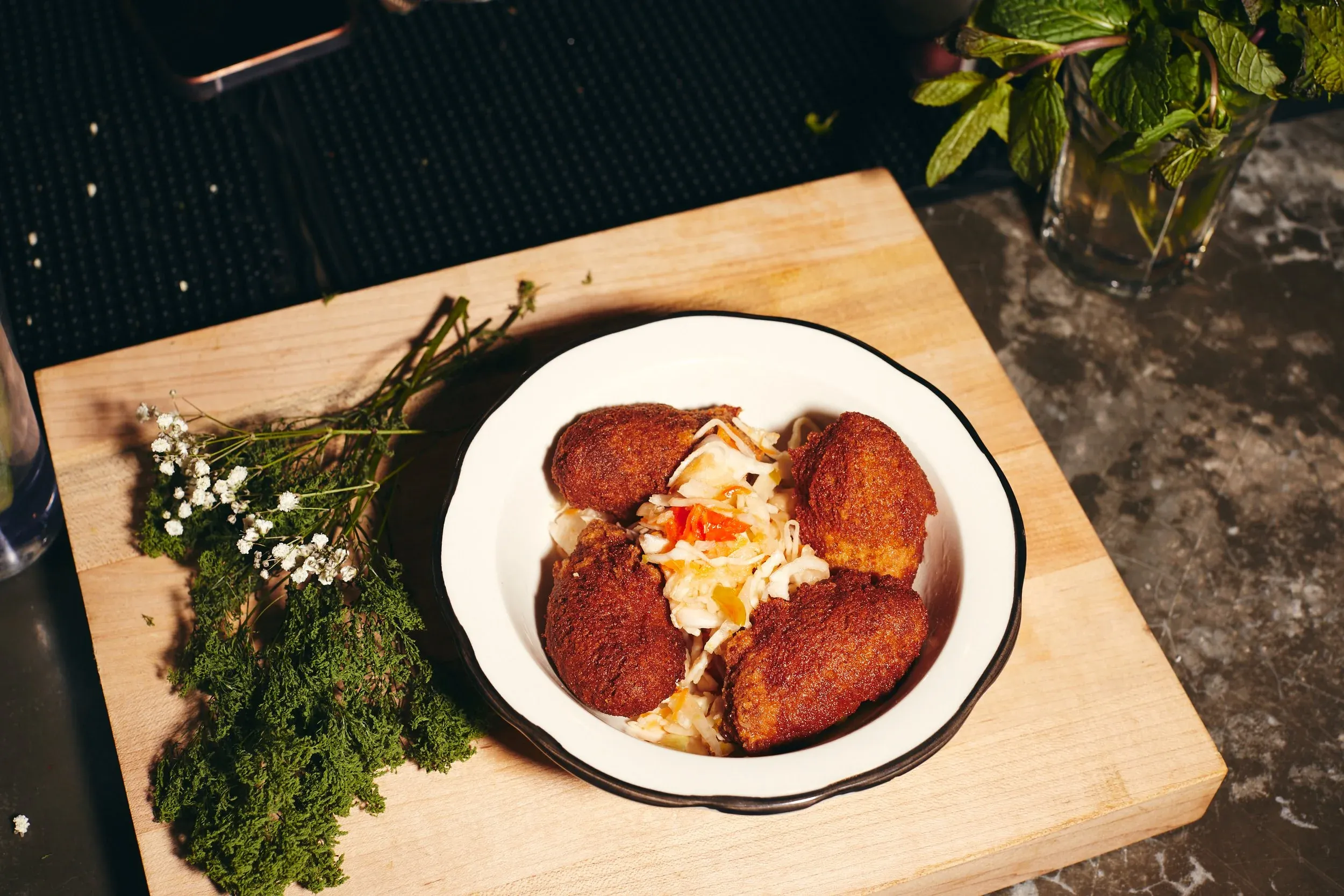 A white bowl of kibbeh and salad on a wooden board.