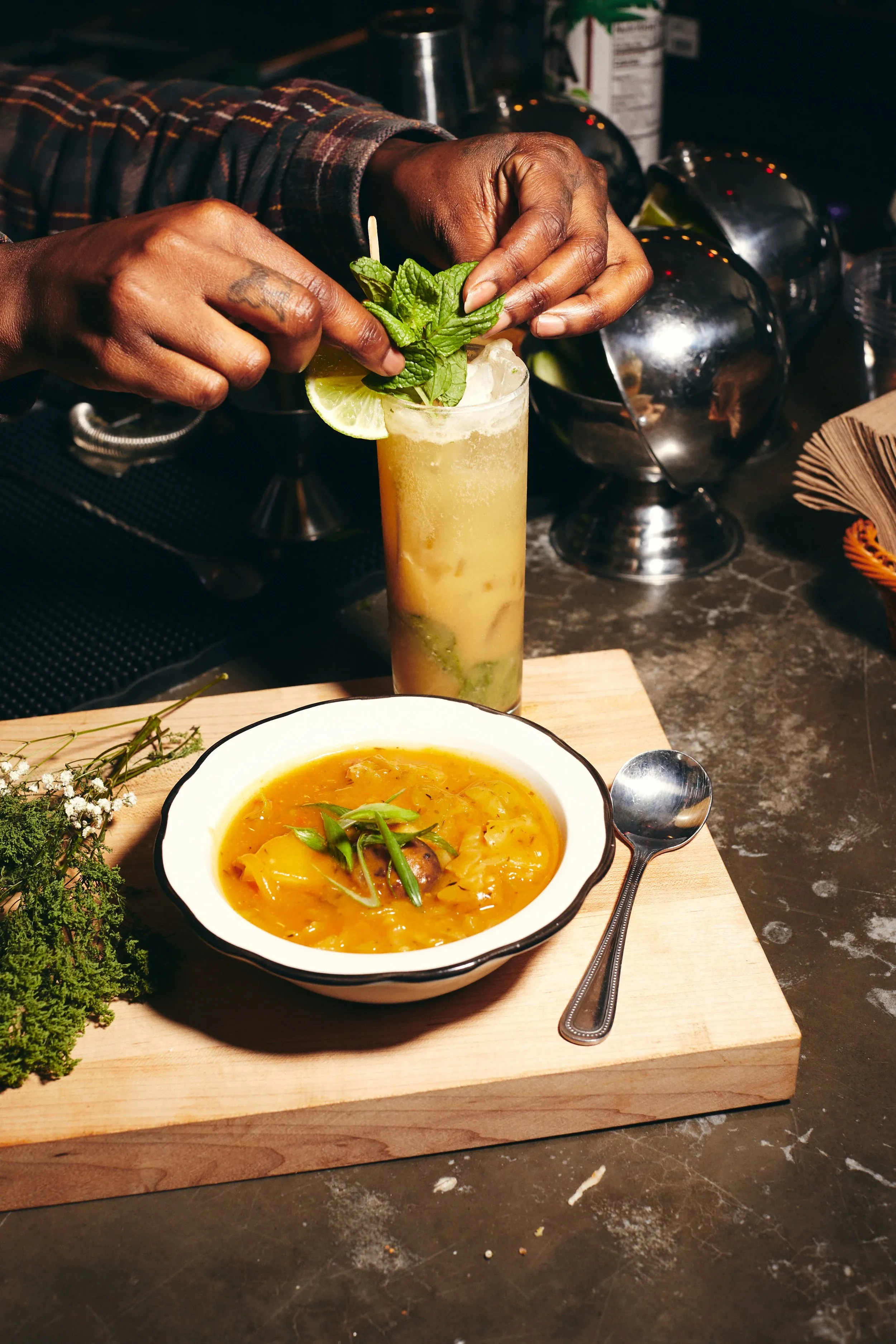A chef garnishes a cocktail next to a bowl of stew.