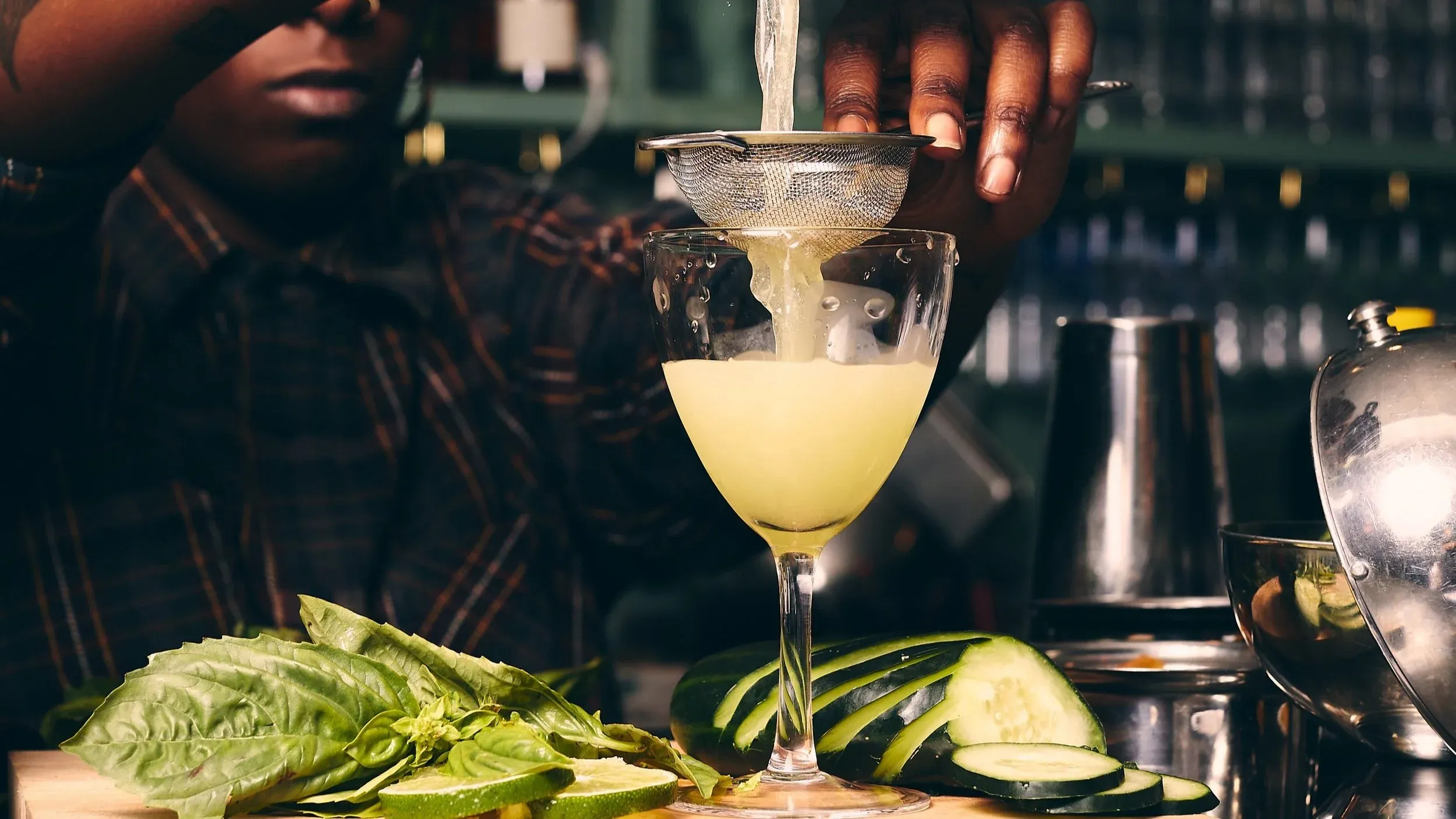 A person straining a light-colored cocktail into a glass.