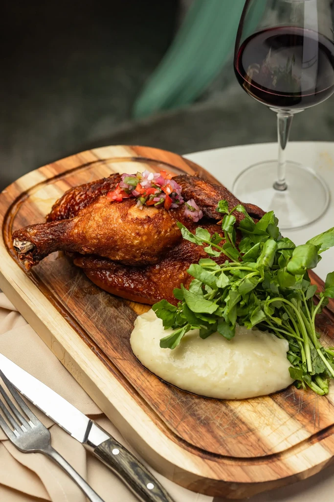 A roasted chicken with salsa, mashed potatoes, and greens on a board.