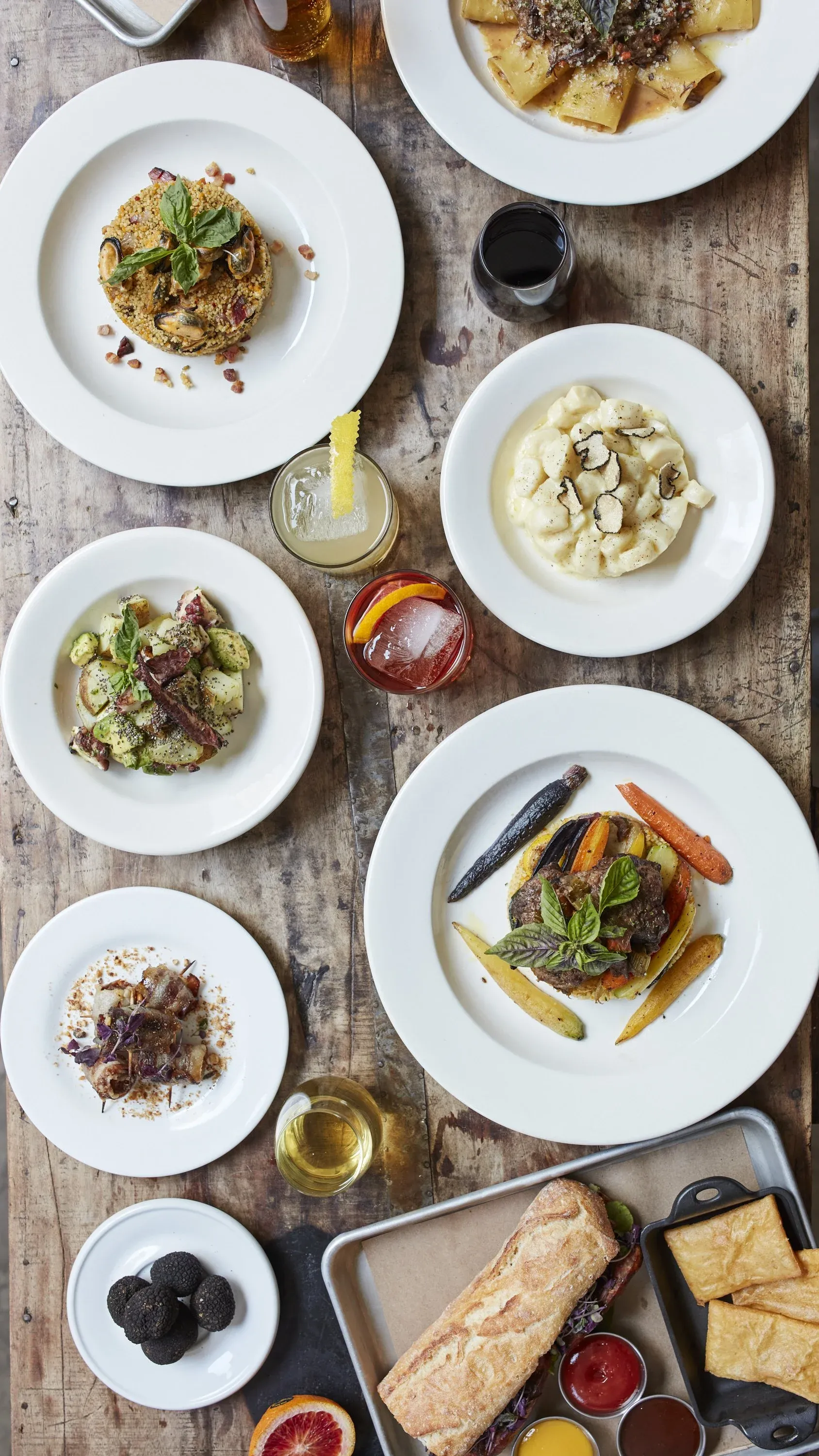 Various dishes on a rustic wooden table with drinks and bread.